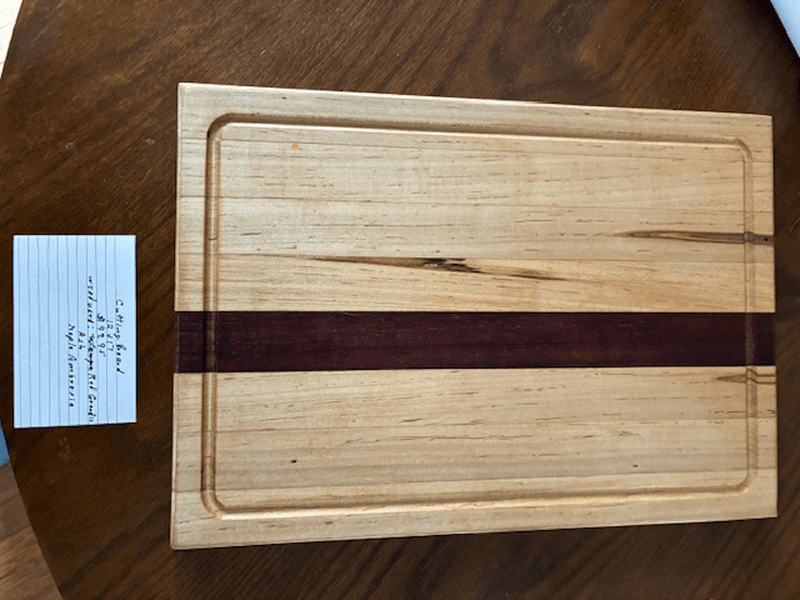 A wooden cutting board with a dark stripe and a groove around the edge.