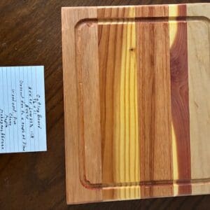 Wooden cutting board with varied wood tones and a note beside it.