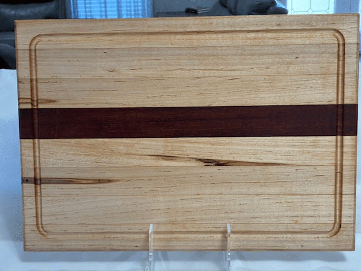 Wooden cutting board with a dark stripe in the middle and a stand.