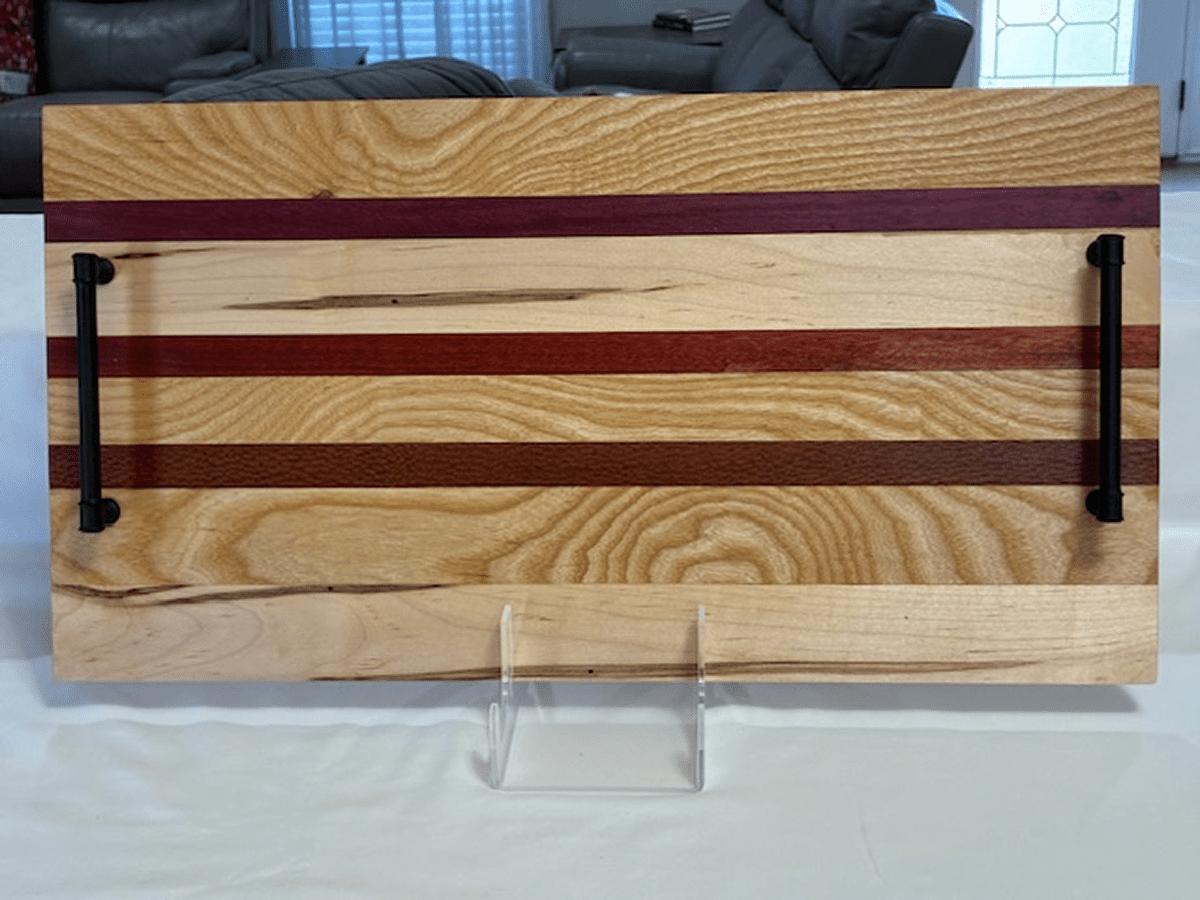 Wooden cutting board with different wood strips on a clear stand.